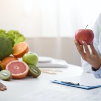 Cropped of nutritionist holding red apple in front of patient